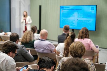 Obraz premium Audience actively participating in a professional presentation with a speaker and slides. Interactive discussions taking place.