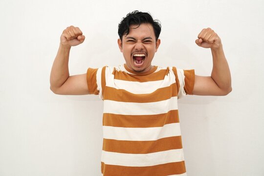 A young Asian man in a white and brown striped shirt shows off his muscles with a happy expression. His energetic pose and confident attitude against a white background.
