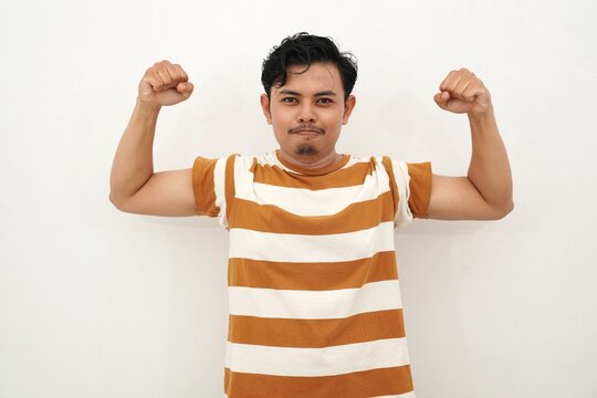 Young Asian man in white and brown striped shirt flexing his arms and shouting with intense facial expression, conveying power or anger, against white background