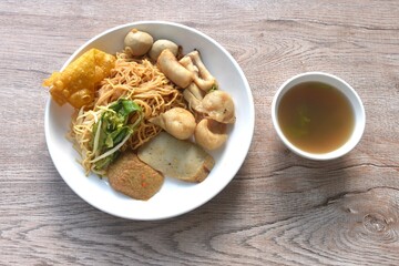 dry yellow egg noodles dory fish and fishball with bean sprout topping crispy dumpling on plate with soup