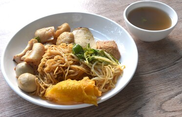 dry yellow egg noodles dory fish and fishball with bean sprout topping crispy dumpling on plate with soup