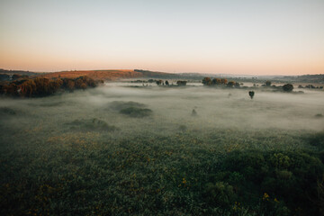 Hot air balloon is flying over foggy landscape at dawn
