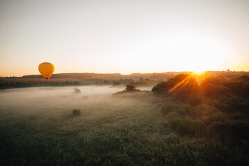 Hot air balloon flying over foggy landscape at sunrise