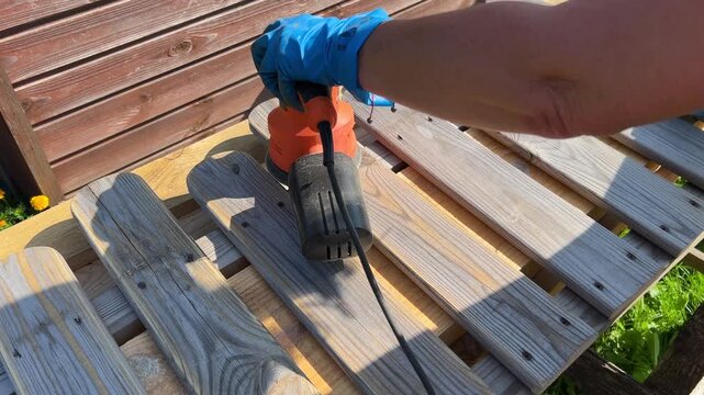 Woman using power tool on wooden pallets in bright outdoor setting during daytime