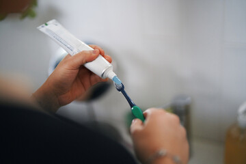 A person's hands are seen squeezing toothpaste from a tube onto a toothbrush. This close-up shot highlights a common daily oral hygiene routine, emphasizing dental care and personal grooming habits.
