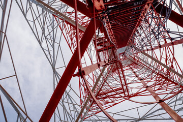 Low-angle view of a red and white telecommunications tower structure against a bright sky, highlighting modern engineering, symmetry, and industrial design.