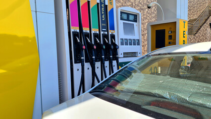 A close-up view of a white car parked at a modern gas station. Fuel pumps are visible in the...