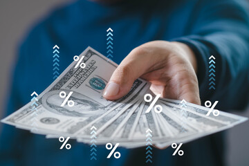 A hand is offering cash bills with percentage symbols and arrows, suggesting concepts of finance,...