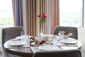 An elegant indoor dining setup featuring white patterned plates, crystal glasses, and a variety of gourmet dishes including salads, stuffed pastries, and cured meats