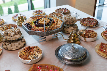 Lavish Middle Eastern dessert table with ornate trays of dried fruits, nuts, baklava, nougat, and sesame treats