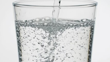 Water is being poured into a glass cup creating bubbles and motion The glass is transparent set against a plain white background - Powered by Adobe