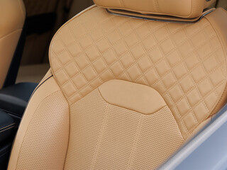 Close-up of luxury car seat with quilted tan leather, perforated lower section and integrated headrest
