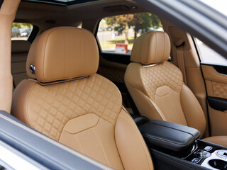 High-end car interior with quilted tan leather seats, perforated ventilation zones and black console armrest