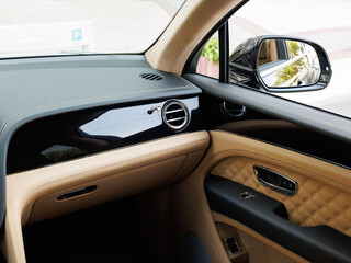 Luxury car interior with tan diamond-stitched leather, chrome air vent and glossy black dashboard panel