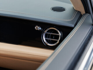 Luxury car dashboard featuring chrome-trimmed circular air vent, beige stitching and two-tone leather finish