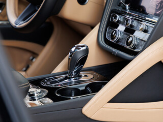 Luxury car interior featuring metallic gear shifter, rotary infotainment dial and chrome-accented control panel