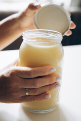 A close-up of a woman hand, featuring light nails, gently opening a large glass jar filled with a...