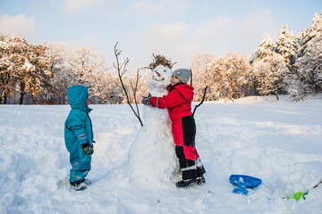 Children hugging snowman in snowy winter wonderland