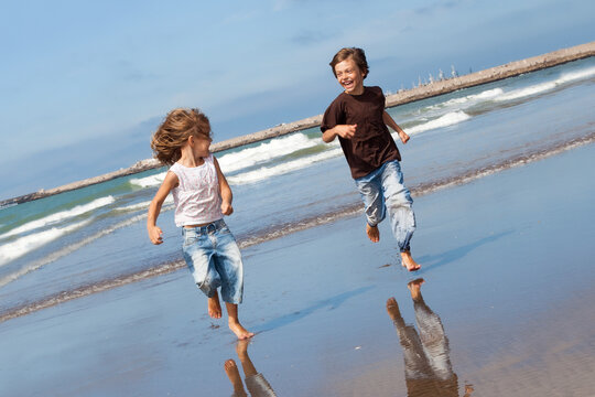 happy kids, boy and girl, running on the beach laughing with ocean in background