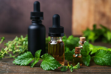 Bottles of essential oil and herbs on wooden table, closeup