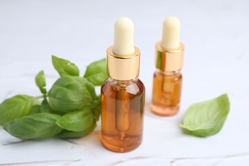 Bottles of aromatic essential oils and herbs on white textured table, closeup