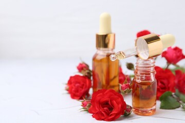 Bottles of essential oil and red roses on white table, closeup. Space for text