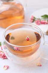 Aromatic tea in glass cup, teapot and roses on light table, closeup