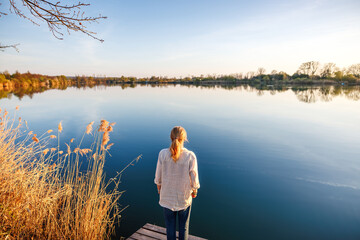 Woman admiring lake horizon during warm golden hour of indian summer in tranquil outdoors scenery. Enjoyment of mindfulness moment in nature
