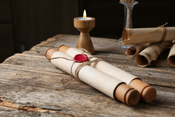 Old paper scrolls and burning candle on wooden table, closeup