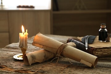 Old paper scrolls, book, feather, inkwell and burning candle on wooden table, closeup