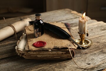 Old paper scroll, book, feather, inkwell and burning candle on wooden table, closeup