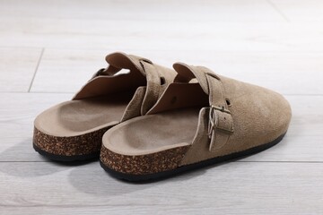 Stylish beige slippers on light wooden floor, closeup