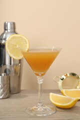 Tasty lemon cocktail in glass and bartender equipment on wooden table against beige background, closeup
