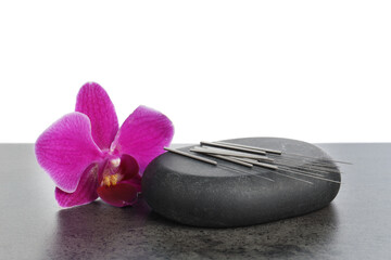 Acupuncture needles, orchid flower and spa stone on grey textured table against white background,...