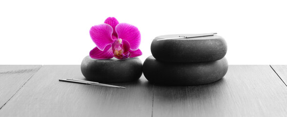 Acupuncture needles, orchid flower and spa stones on grey wooden table against white background,...