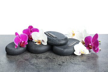 Acupuncture needles, orchid flowers and spa stones on grey textured table against white background