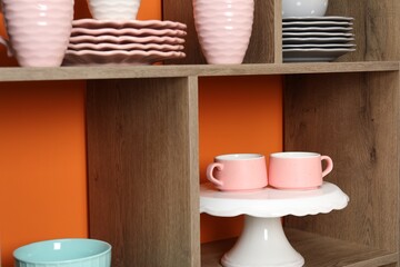 Shelving unit with different dishware and cups near orange wall indoors, closeup