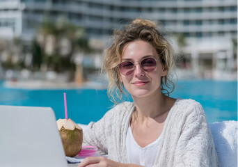 Young woman enjoying remote work by the poolside with laptop and coconut drink, embodying the freedom of digital nomad lifestyle