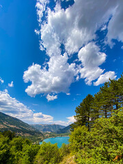 Scenic Lake Scanno nestled among verdant greenery, panoramic landscape revealing crystalline waters beneath azure sky with floating clouds