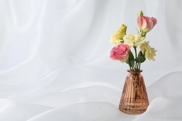 Beautiful flowers in glass vase on white cloth, space for text