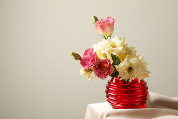 Beautiful flowers in glass vase on beige cloth against light background, space for text