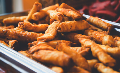 Close-up of a metal tray brimming with numerous crispy, golden-brown fried spring rolls, creating an enticing display at a buffet or catered event