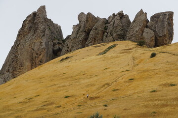 A man on a path leading up a golden hillside with rocks and a building on the Besh Barmag Mountain...