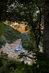 Naklejka premium Warm sunset illuminating a charming italian village nestled in a valley, seen through a frame of trees