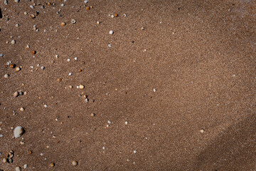 Beach surface fills foreground with fine sand grains and scattered pebbles and shells. Earthy tones create serene mood, perfect for nature and travel projects.