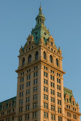Majestic historic skyscraper reaching towards the sky, showcasing intricate architectural details and a distinctive patinated green roof under a clear blue sky, a timeless urban landmark.