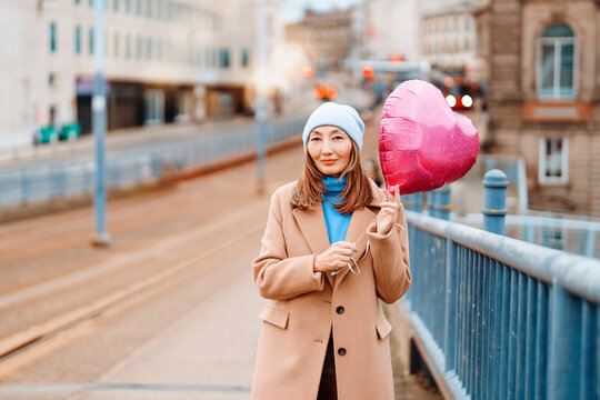 Asian woman enjoying a red balloon while walking in a modern urban space during the day