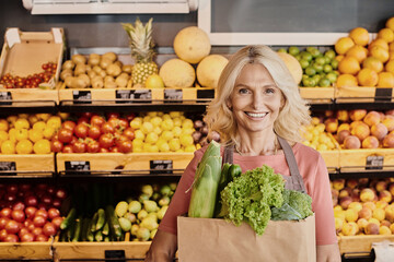 Blonde saleswoman showcases fresh organic produce in a bustling grocery store