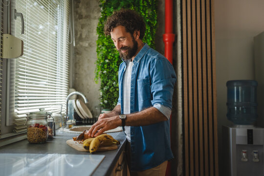 Smiling man slicing banana bread in modern kitchen