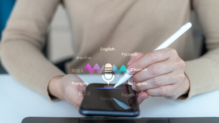 Close-up hand using a smartphone with a microphone icon and multiple languages. Concept of AI voice recognition, real-time translation, and global communication.